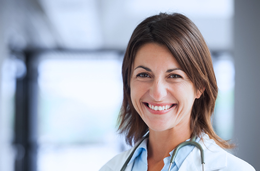 Close-up of a healthcare provider smiling toward a camera with a light and blurry background.