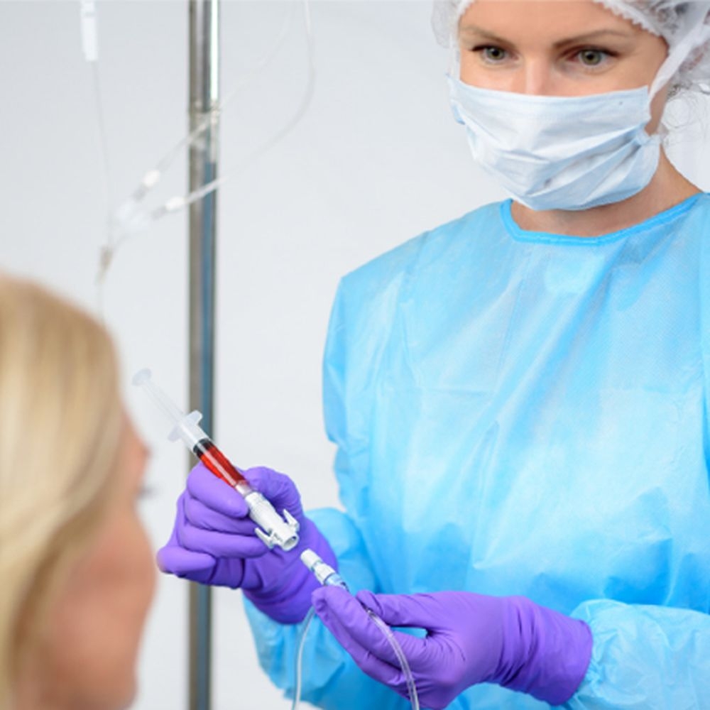 Nurse with a mask and dressed in protective clothing looking at patient while holding OnGuard 2 CSTD.