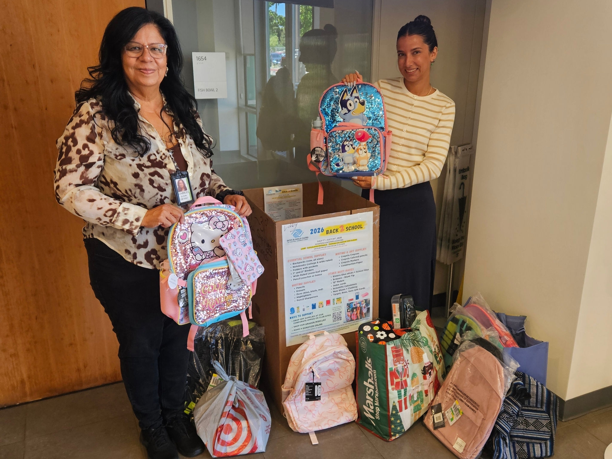 Two B. Braun employees stand beside a collection of donated backpacks and school supplies during a Back 2 School Drive, supporting local students and families in the community.