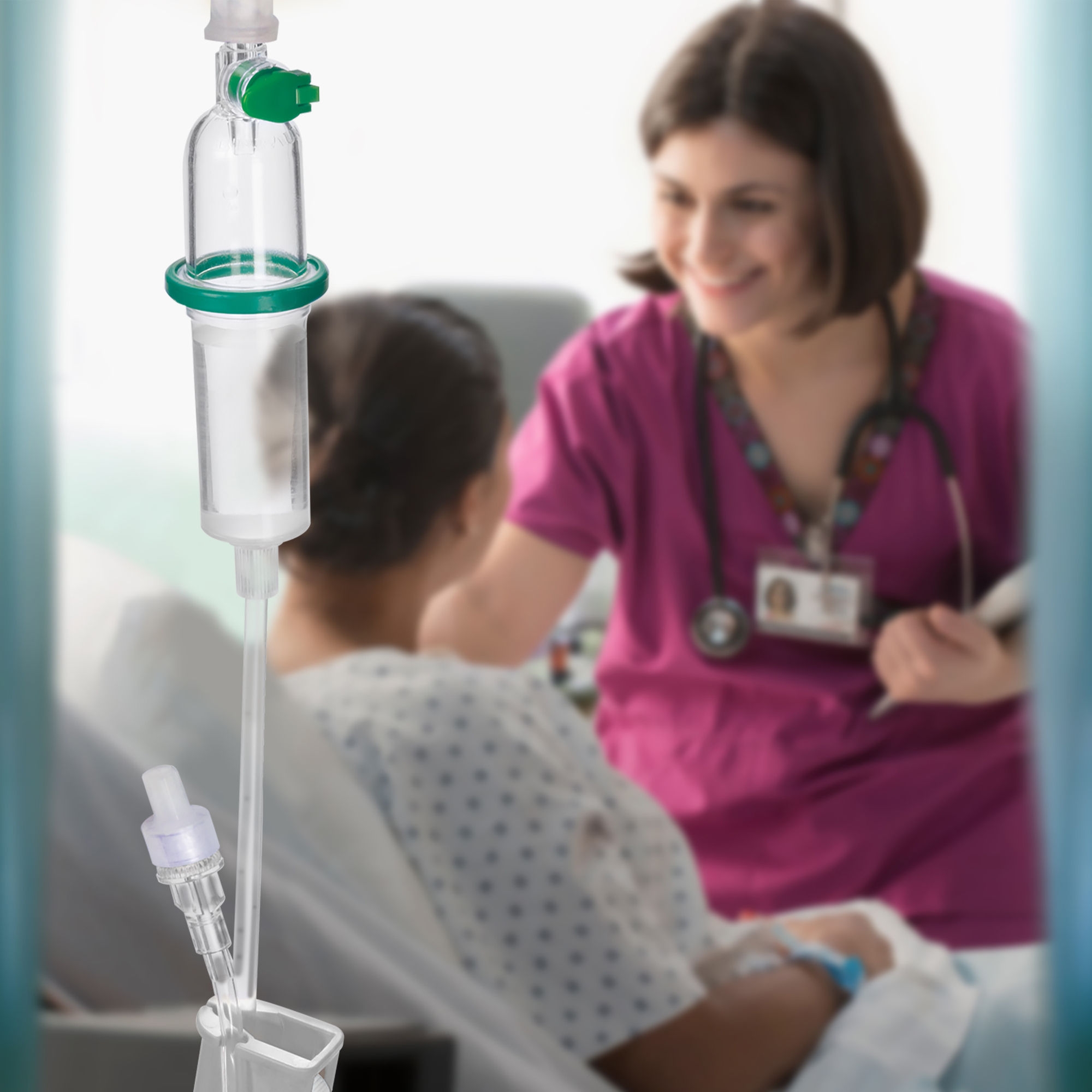 A female nurse holding a clipboard attends to a female patient in hospital, with a portion of a B. Braun IV set in the foreground.