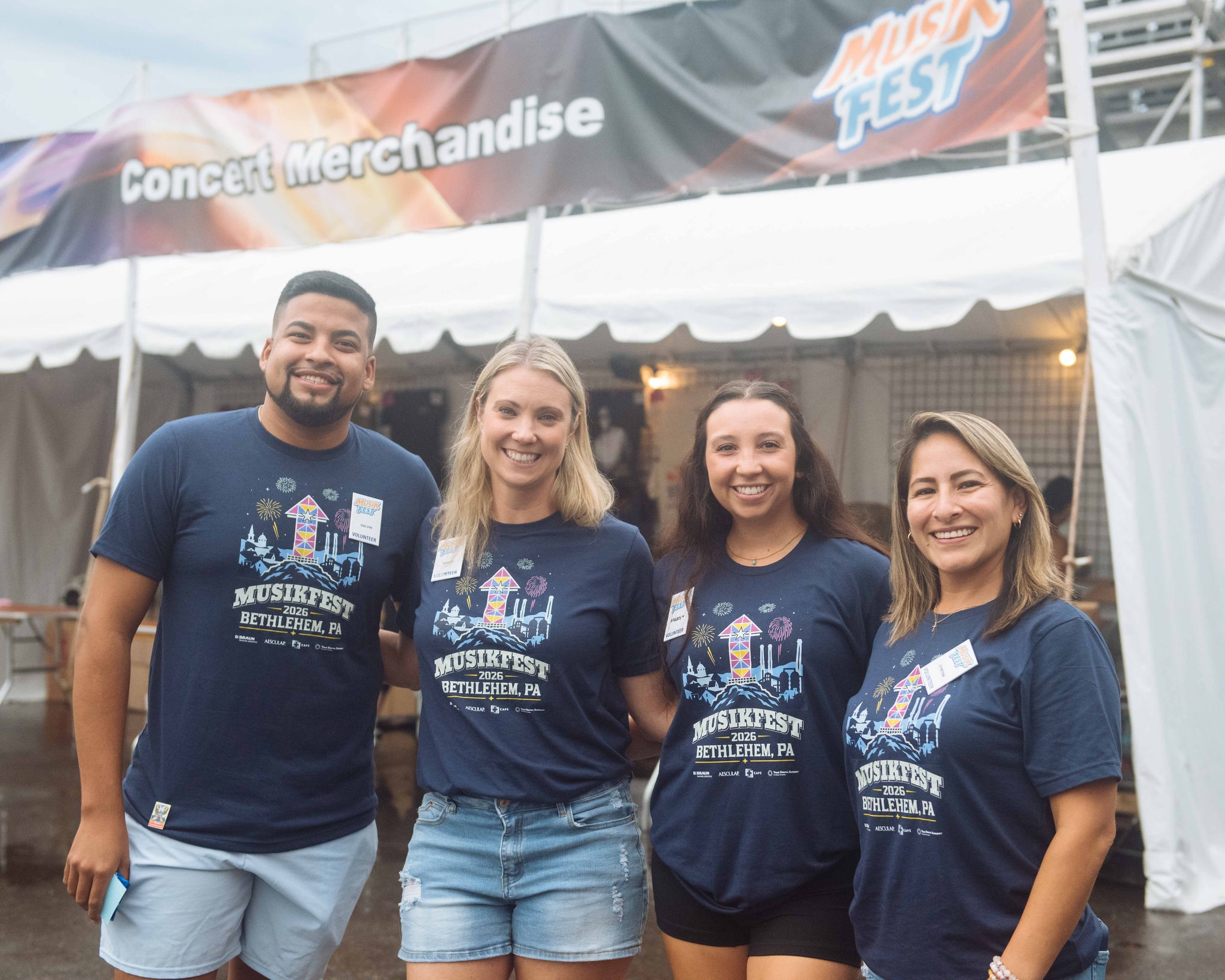 Four B. Braun employees wearing Musikfest 2026 shirts pose in front of a Musikfest merchandise tent, representing the ASPIRE Employee Resource Group during the community festival in Bethlehem, PA.