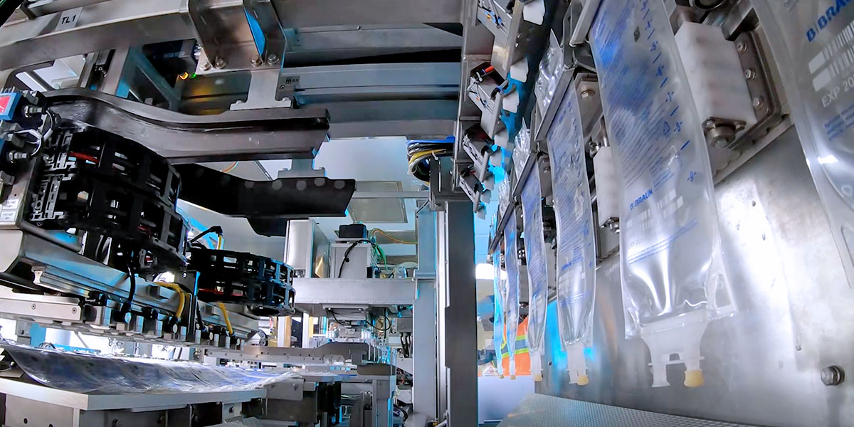 A close-up view of an industrial machine, which is part of a manufacturing assembly line. The machinery is complex, with various metal components, wires and blue light.