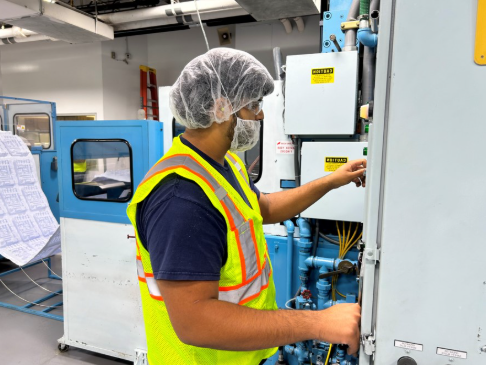 Employee wearing safety gear operating industrial equipment in a manufacturing facility.