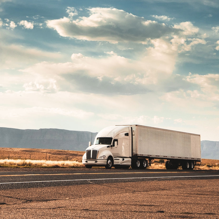 A large white semi-truck driving down the highway in what appears to be the plains of middle America.