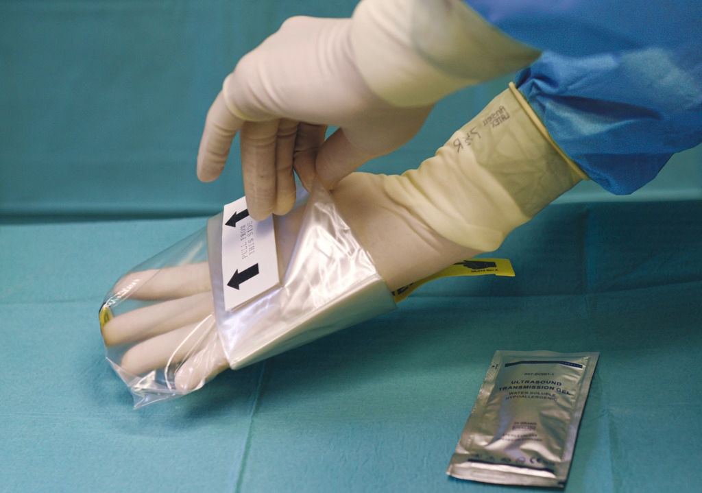 A person wearing medical gloves pulls an EZCOVER Probe Cover Set over their hand, with a "PULL HERE" label, against a teal background.