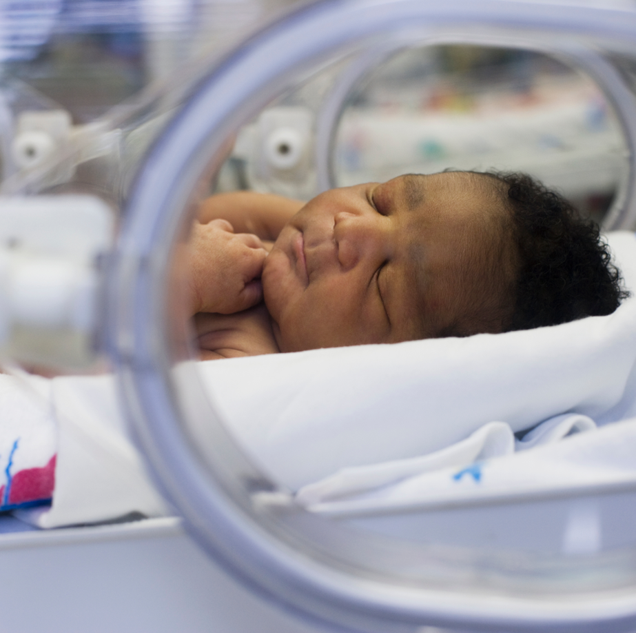 An infant boy in the NICU sleeps in an incubator.