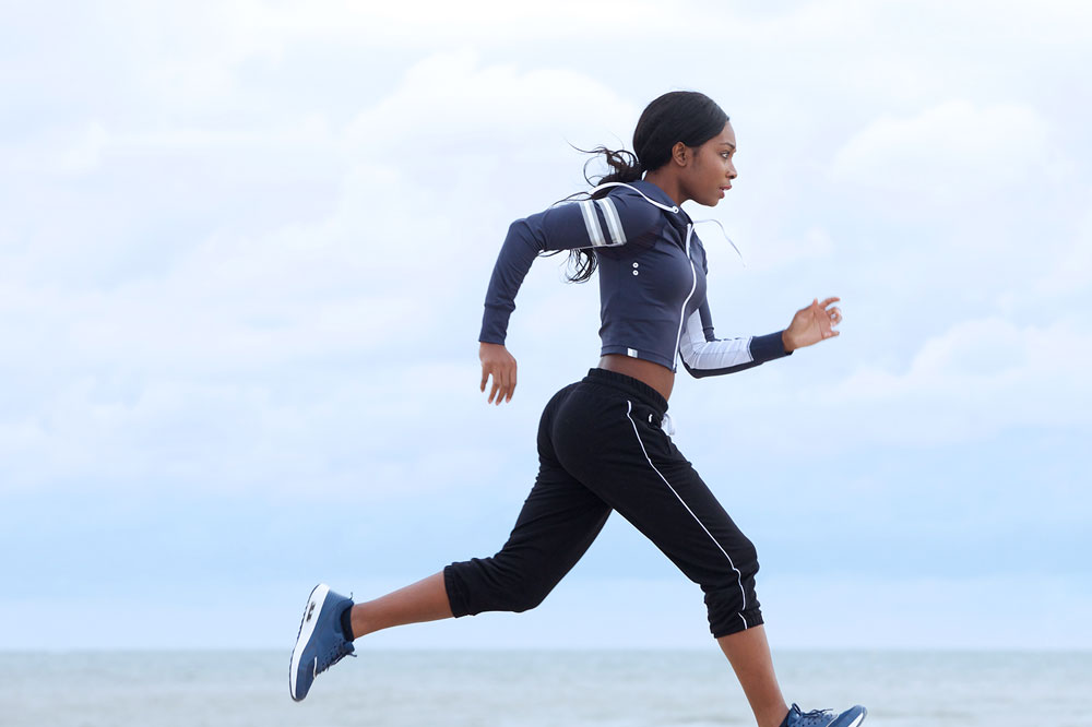 Woman running outside on a beach under cloudy skies.