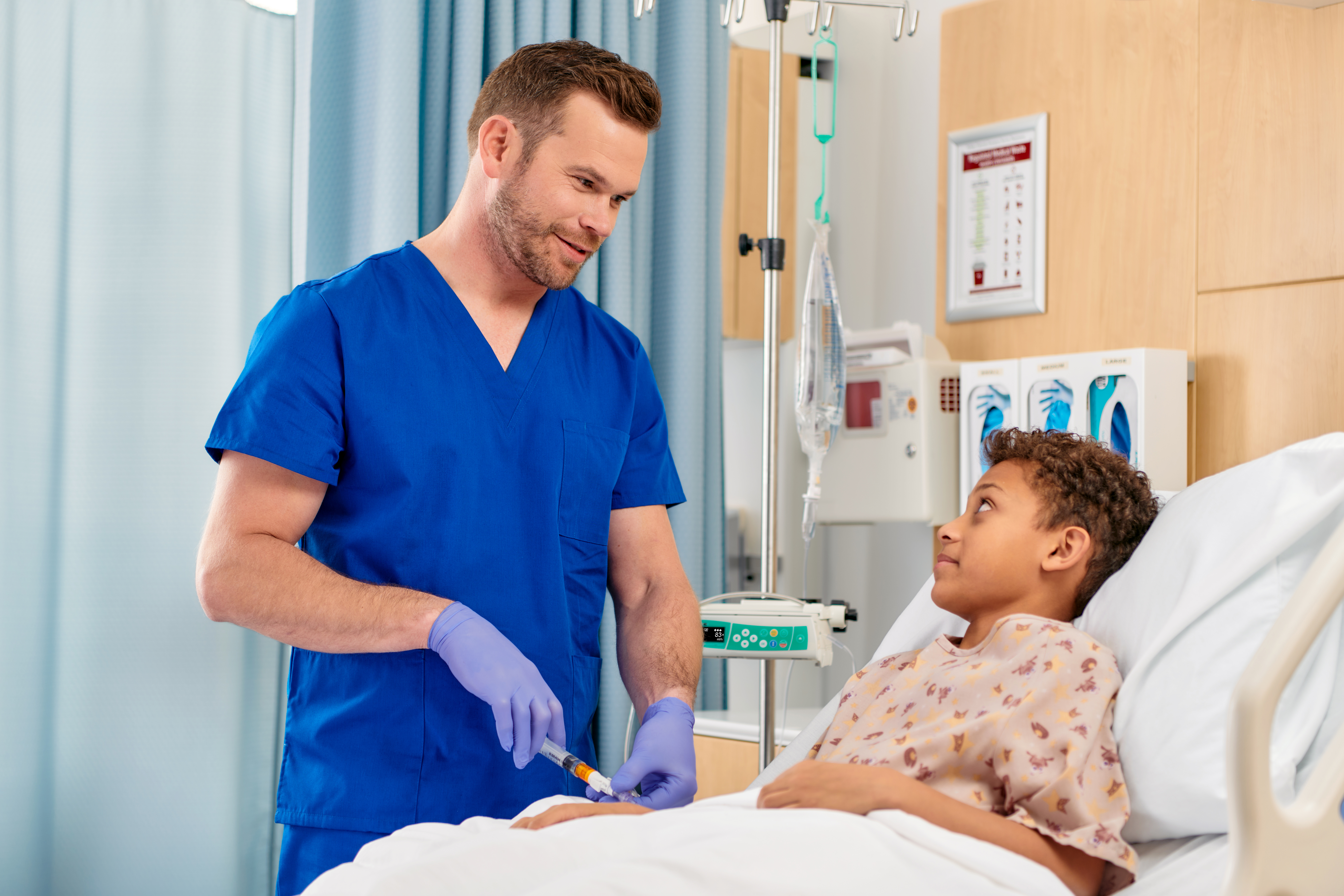 A healthcare provider administers an injection to a young patient sitting in a hospital bed.