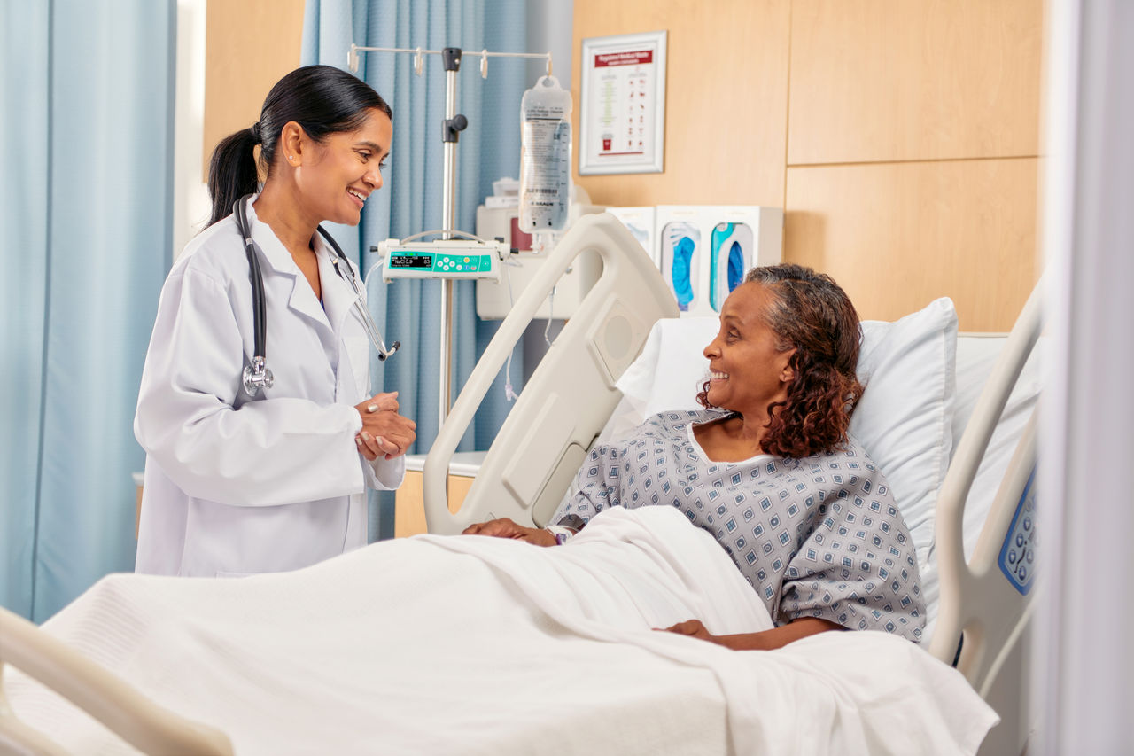 Patient, resting in a hospital bed, smiles up at a healthcare provider.