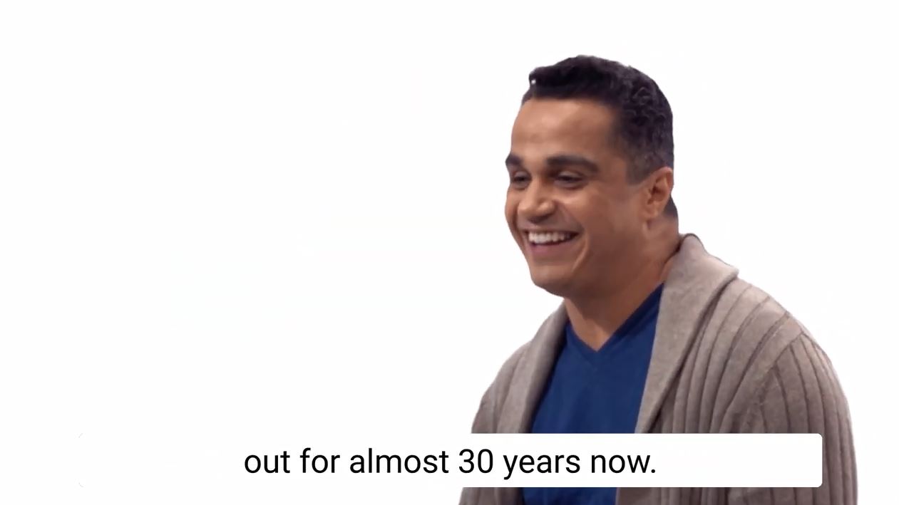Employee and member of the LGBTQ+ Employee Resource Group sitting with a white background and facing off camera as he smiles.