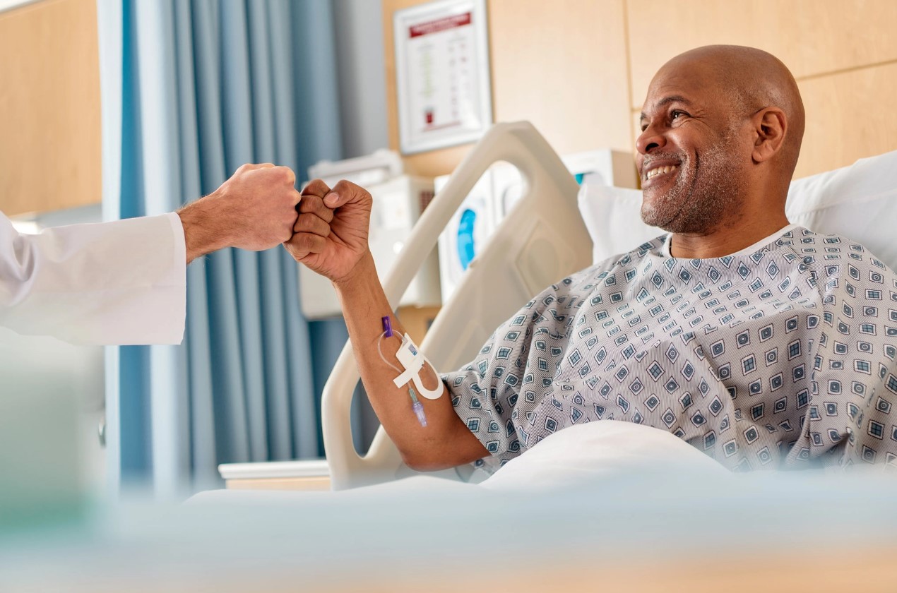 Smiling patient reclines in hospital bed and fist bumps a provider.