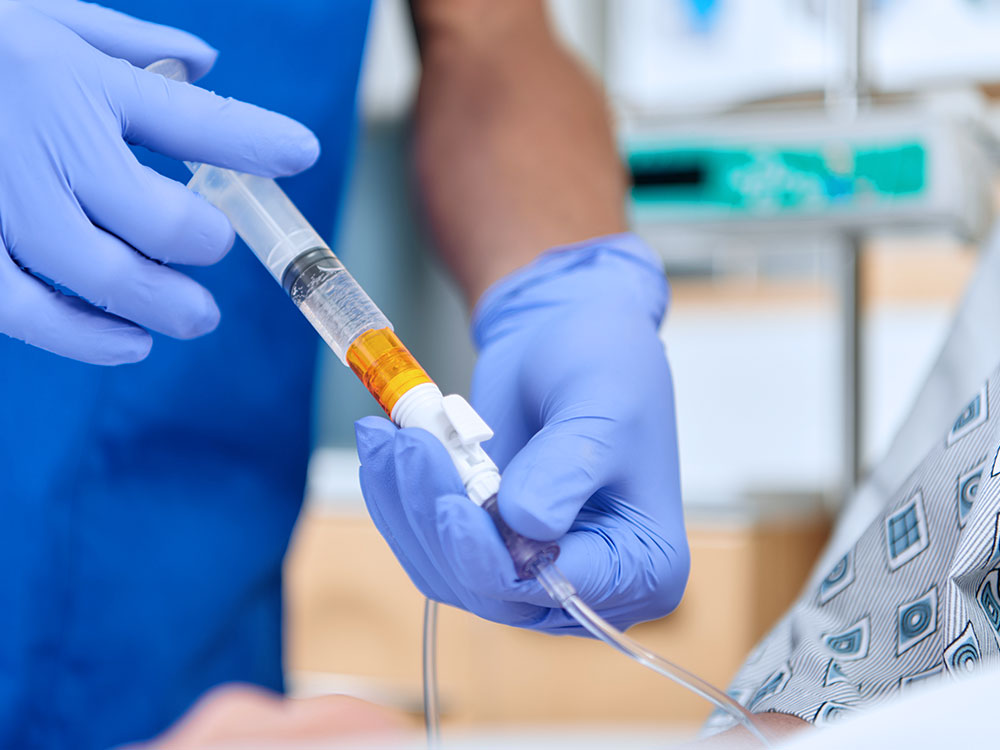 A provider wearing blue gloves connects OnGuard 2 CSTD to administer a hazardous drug. 