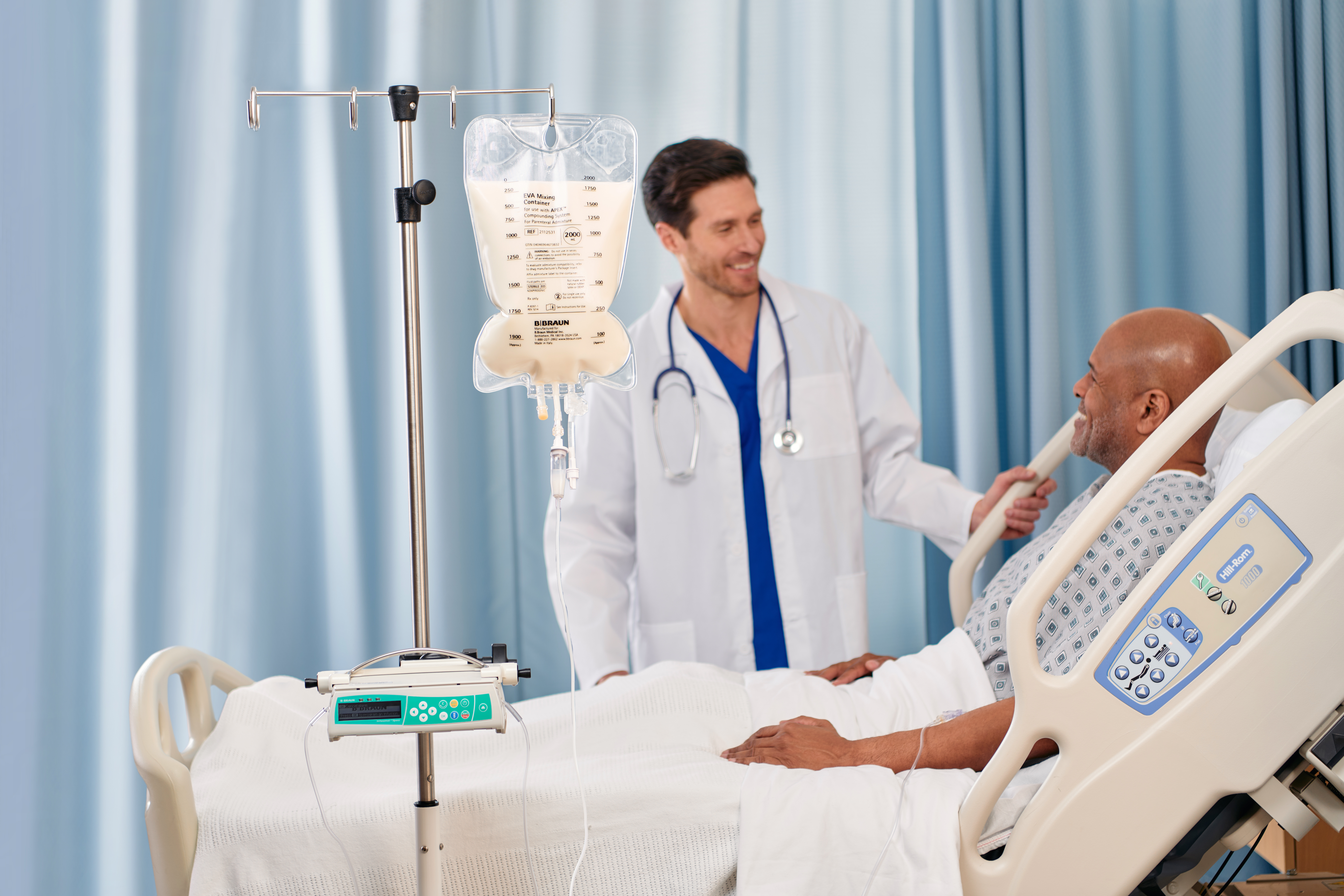 Patient reclines in a hospital bed while talking to a provider with an IV pole and container beside the bed.