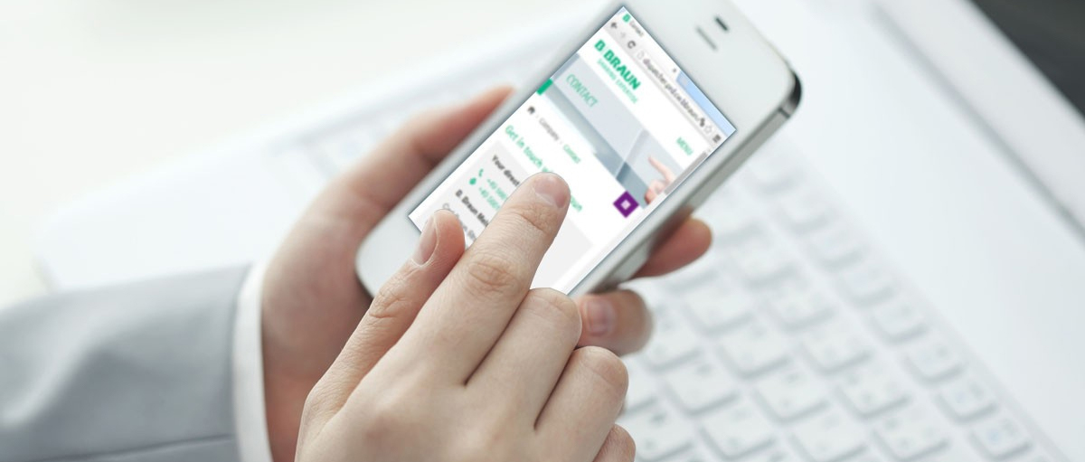 Hands hold an iPhone while scrolling on the B. Braun Medical Inc. website.