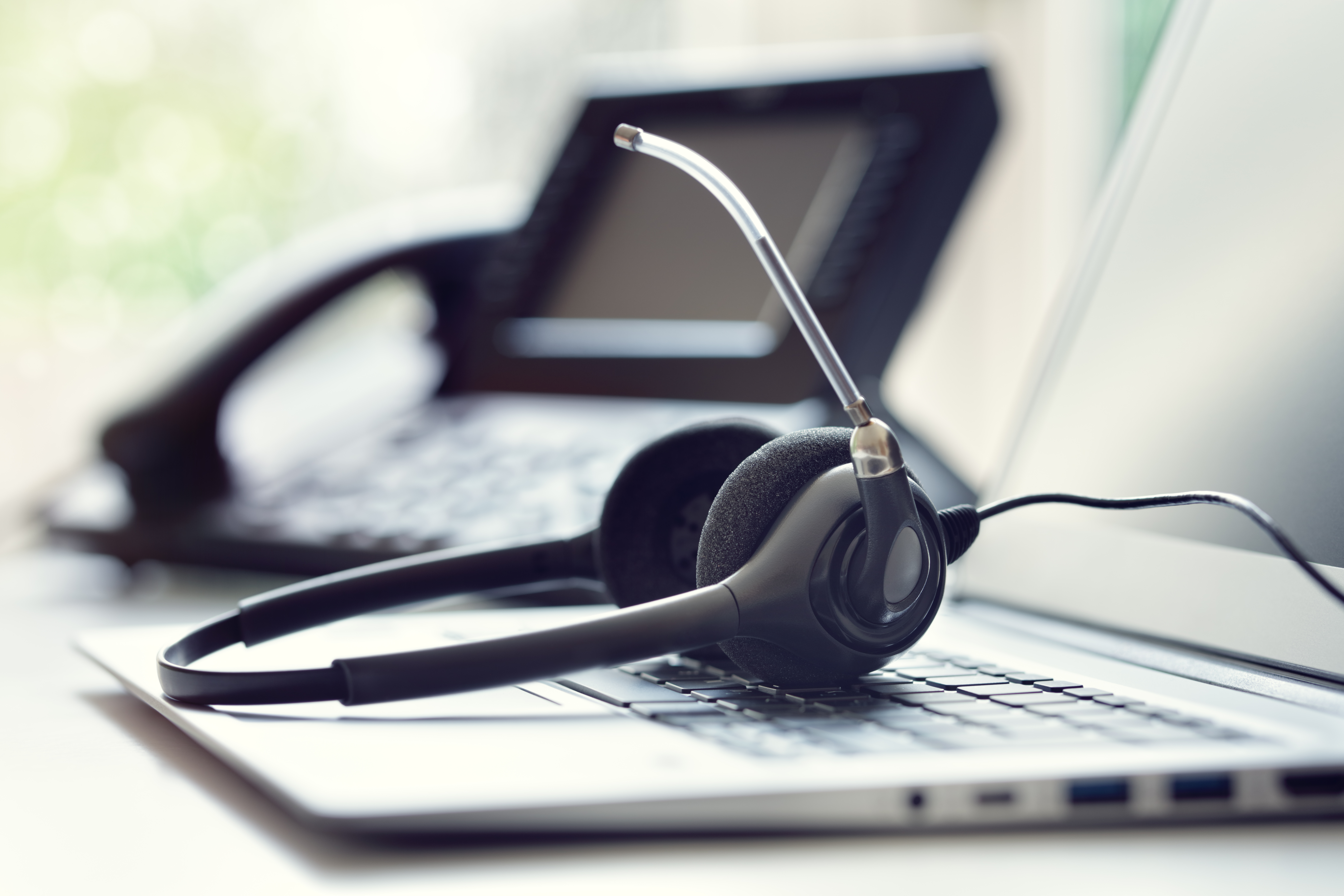 A headset sits on an open laptop with a phone set in the background.