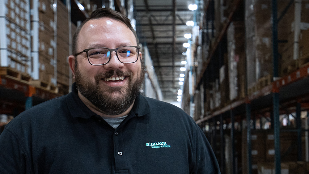 B. Braun employee wearing a company shirt smiling toward the camera in a B. Braun warehouse.