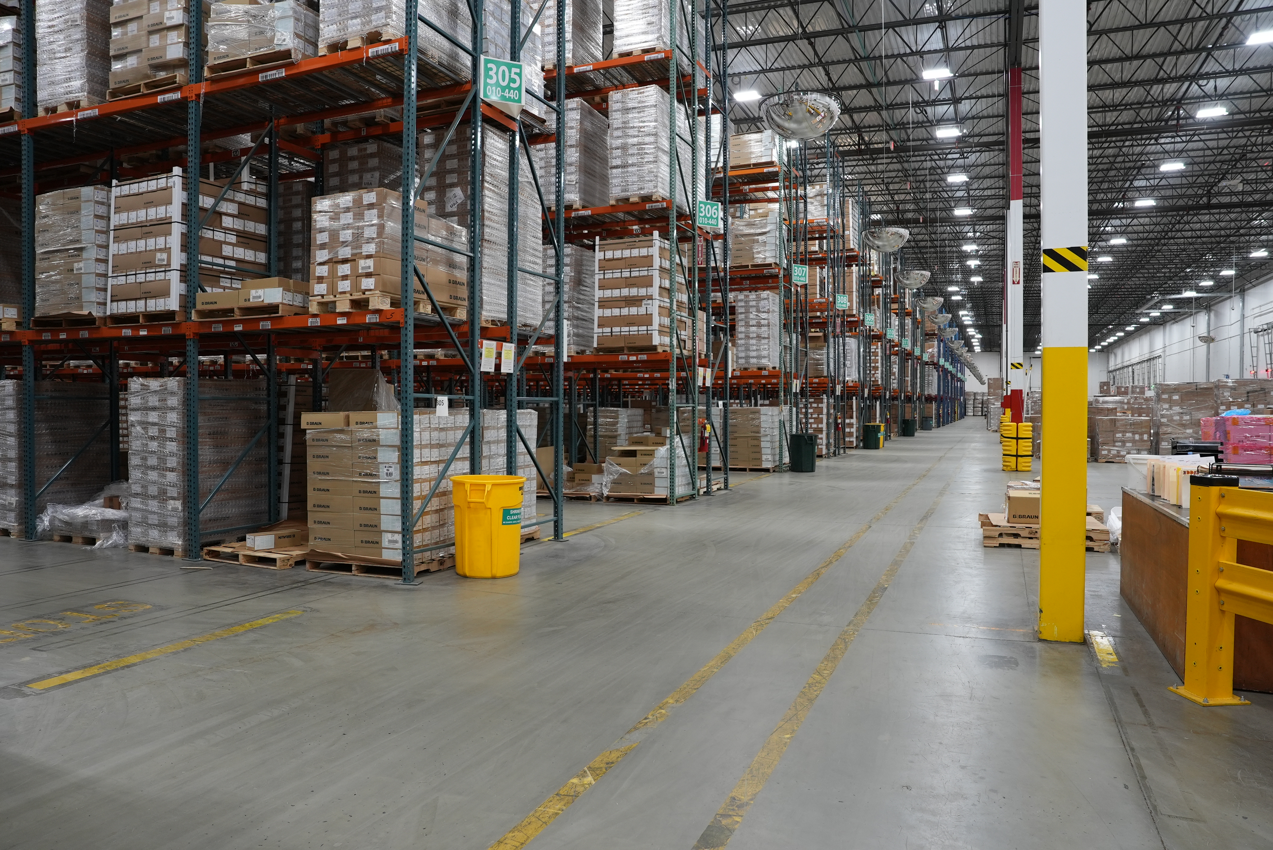 Wide shot inside a B. Braun distribution facility, with rows of tall shelves stacked with boxes.