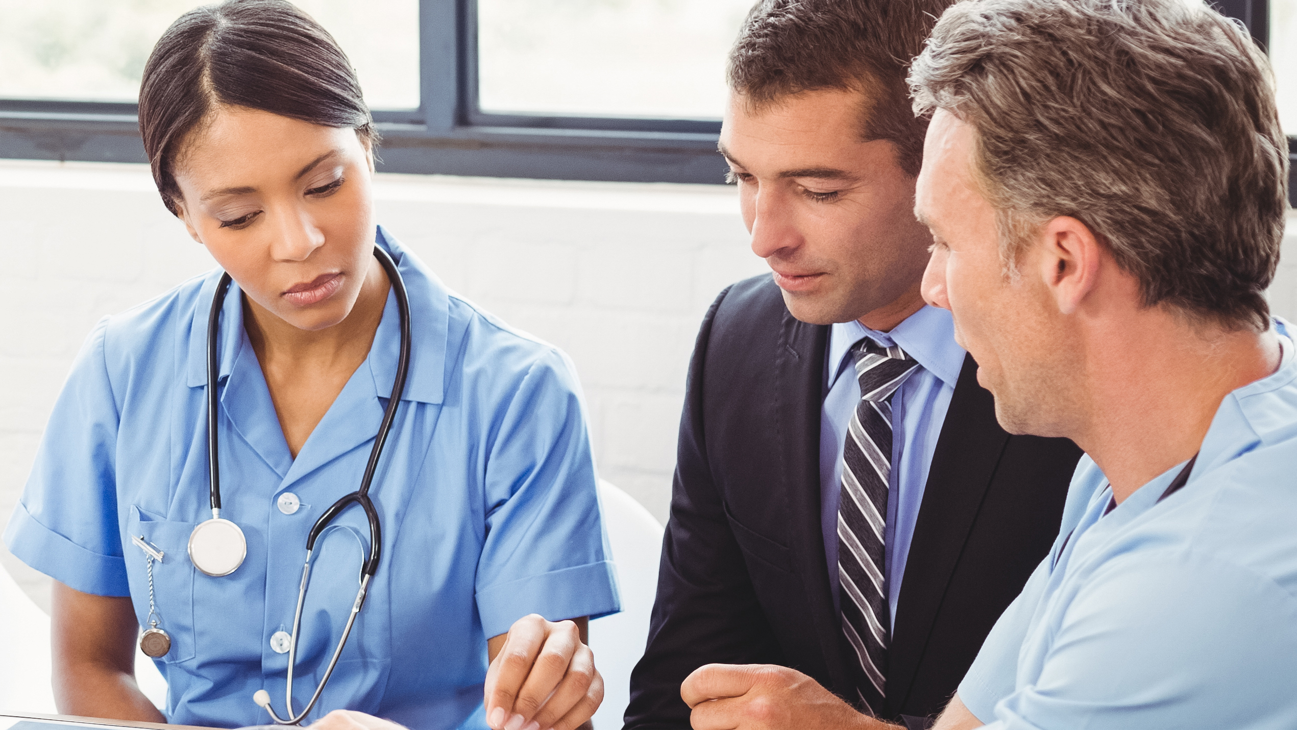 Two providers sit with a man in a suit as they look over paperwork that's before them.