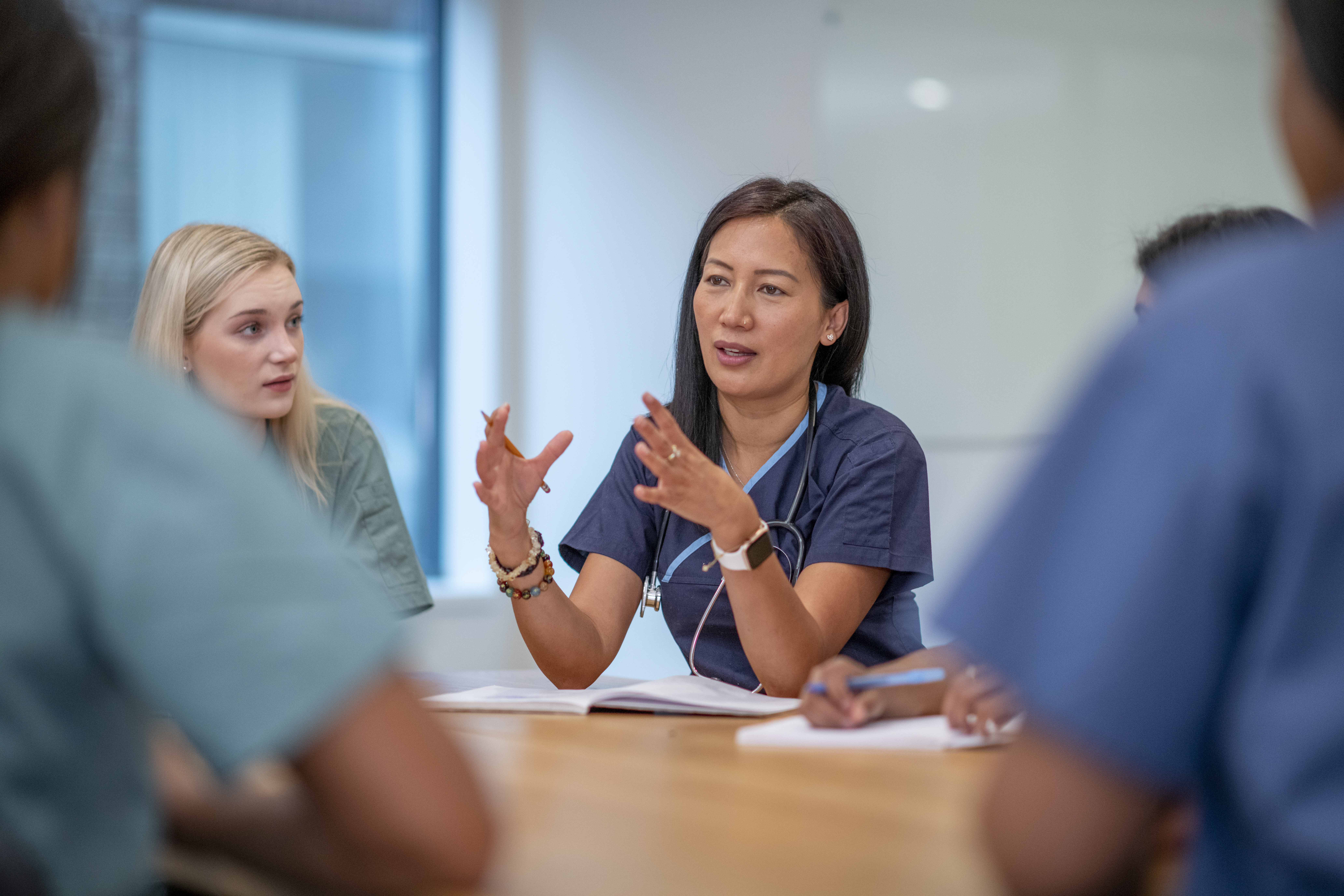 Several healthcare providers sitting at a table with the focus on one provider, speaking to the rest of the group in a learning setting.
