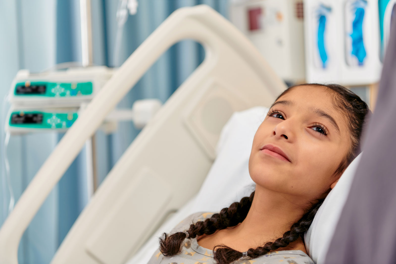 A young patient lying in a hospital bed with an Infusomat Space Large Volume Infusion Pump and Perfusor Space Syringe Pump in the background.