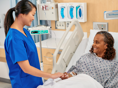 Female patient smiling up at a nurse as she rests in hospital bed.
