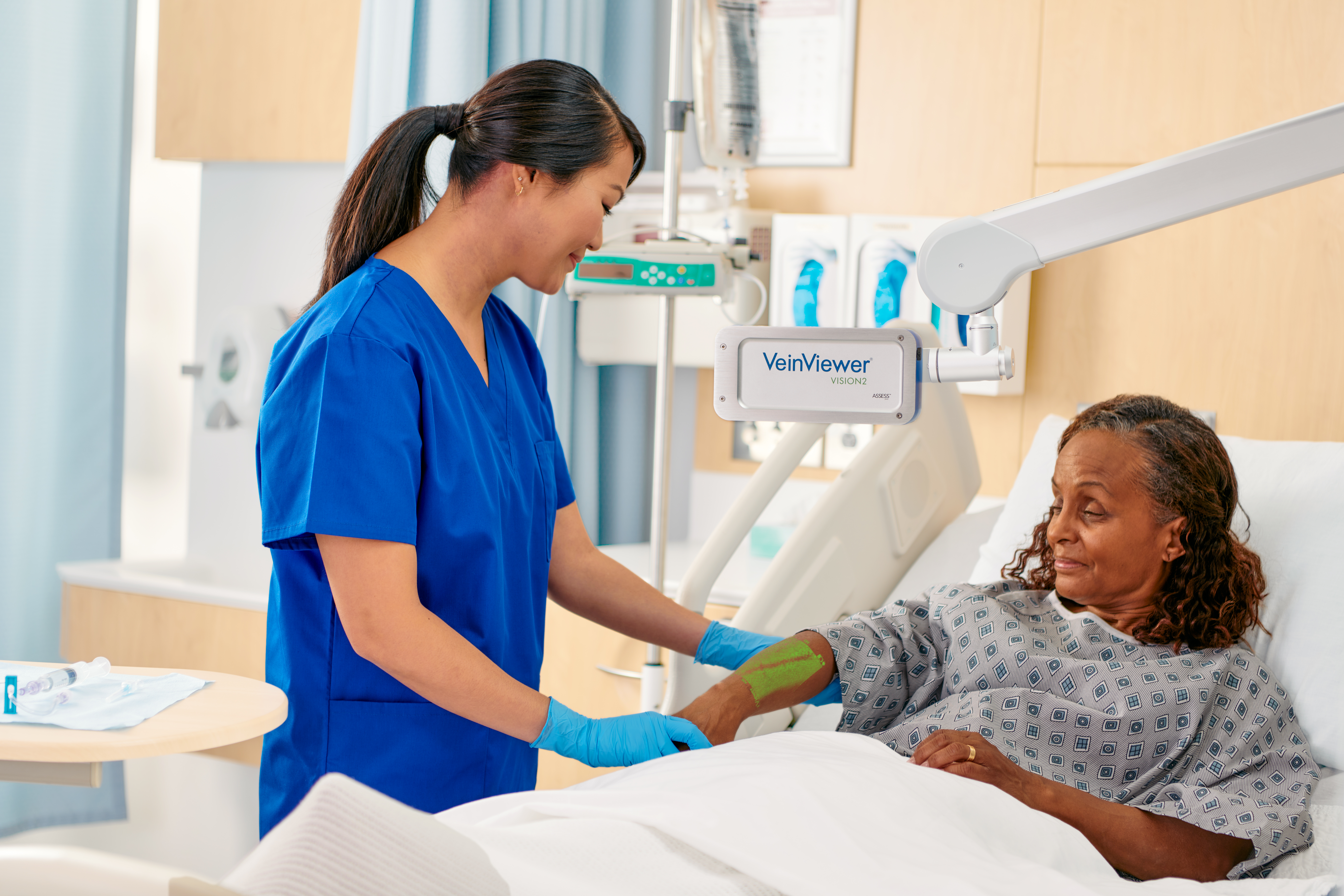 A nurse in blue scrubs uses the VeinViewer Vein Visualization Device to location a patient's veins. 
