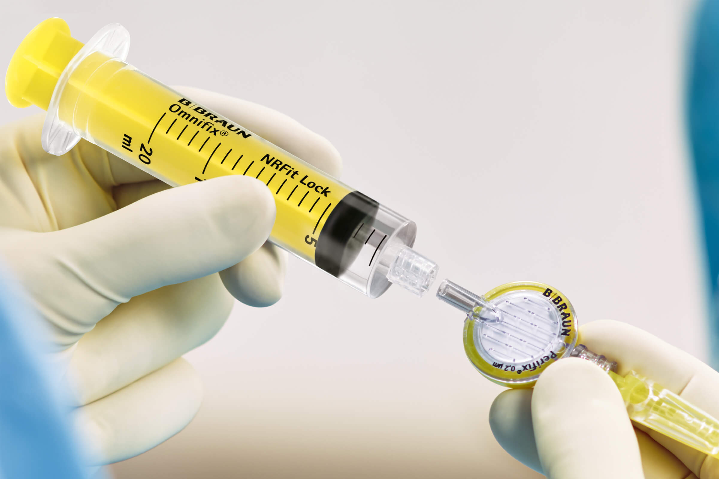 Hand with white glove holding a NRFit Syringe connecting it to a NRFit Epidural Filter.