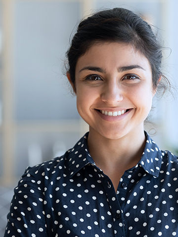 Woman wearing polka dot blouse smiling with an office background.